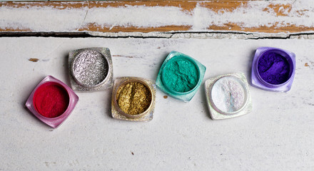 Different color nail glitter on the wooden table with shells and