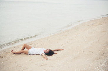 Young woman with white t-shirt lying down on the beach. Smiling