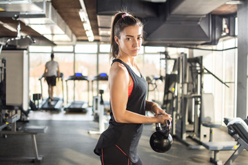 Fototapeta na wymiar Attractive sporty girl doing exercises with kettlebell in a gym.