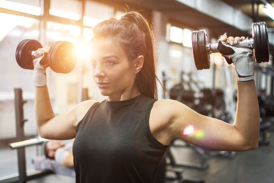 Beautiful young woman working out with dumbbells in gym.