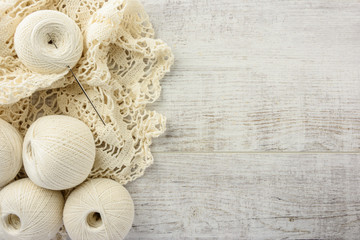 crochet tablecloth, crochet hooks and balls of cotton thread on a white wooden table. top view,...