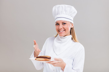 Beautiful female confectioner is showing slice of cake on gray background.
