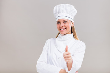 Portrait of beautiful female chef showing thumb up on gray background.
