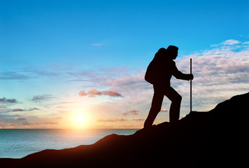 Ascent climber on top of a mountain on a background of sea sunset.
