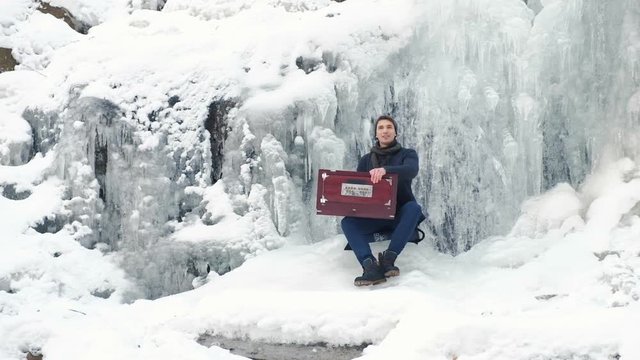 Happy young man playing the harmonium on a frozen waterfall