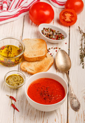 Delicious tomato soup with spices and fresh herbs. Olive oil, pepper, tomatoes, thyme and toasted bread on the table. Selective focus
