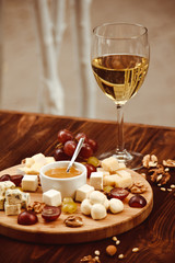 Cheese Board served with grapes, nuts and a glass of white wine on a wooden background