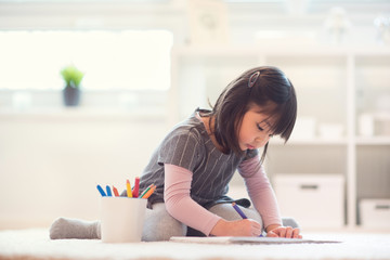 Pretty happy little japanese girl drawing with pencils at home