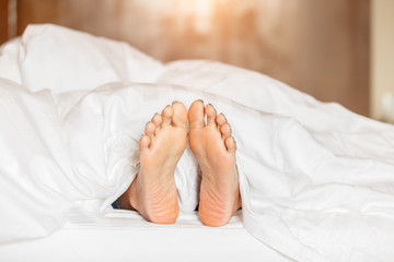 Woman feet under white blanket side view. Beautiful young woman feet with blue pedicure on the bed. Sleeping woman legs under the white blanket
