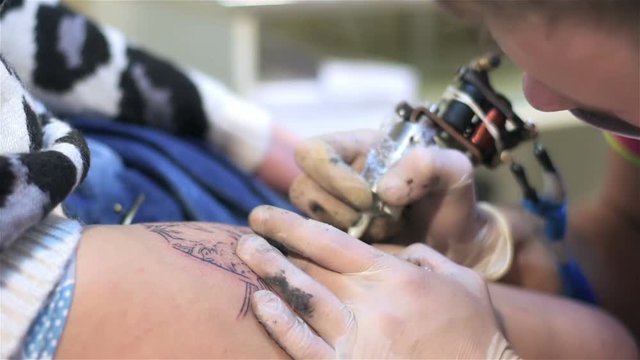 Guy fills tattoo on body. Close up. Tattoo parlor. Patterning on skin. Body art