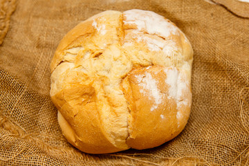 Homemade round bread from wheat flour lies on rough cloth..