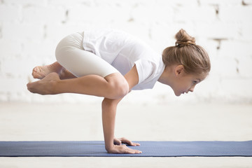 Side view of Girl child practicing yoga, standing in Crane exercise, Bakasana pose, working out...