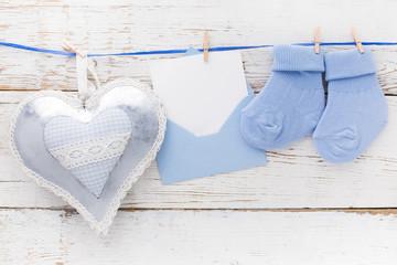 Small boy blue socks, blank card in evelop and heart on white wooden background. Flat lay.