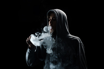 One man in the hood vaping e-cigarette and blowing a cloud.