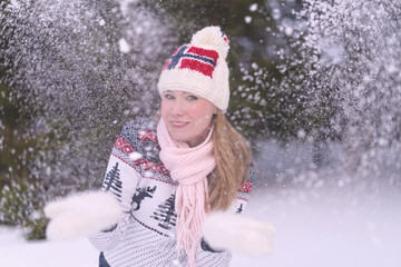 Woman in hat with Norway flag and scandinavian sweater has fun in winter forest. Blowing snow