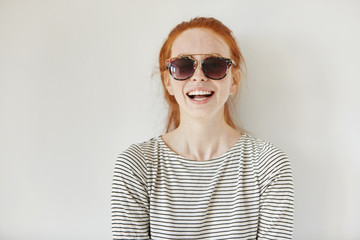 Headshot of happy beautiful fashionable young redhead woman wearing trendy sunglasses and striped...