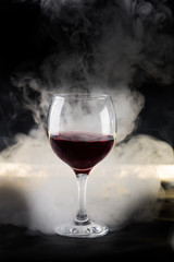 glass of red wine on black background with backlighting and smoke