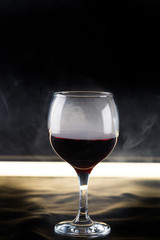 glass of red wine on black background with backlighting and smoke