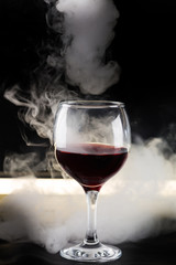 glass of red wine on black background with backlighting and smoke