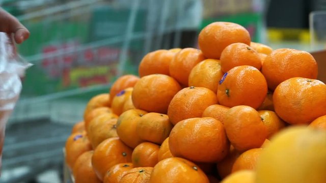 Hand picking orange and put in bag. Fresh fruits selling in supermarket