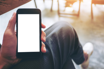 Mockup image of hand holding black mobile phone with blank white screen on thigh with white canvas shoes