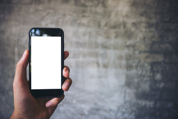 Mockup image of hand holding black mobile phone with blank white screen on concrete polishing wall background 