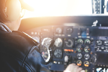 Caucasian captain piloting airplane. Backview of professional aviator in sunglasses and outfit flying Boeing aircraft, getting ready for departure, sitting in cabin with sun shining through windscreen - obrazy, fototapety, plakaty