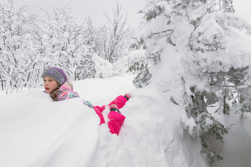 Маленькая девочка лежит в глубоком снегу.