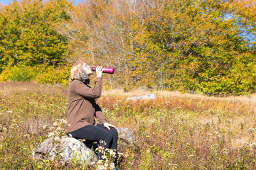 Young woman sitting on rock in meadow drinking water from bottle