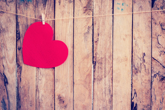 Red heart hanging on clothesline and rope with wooden background