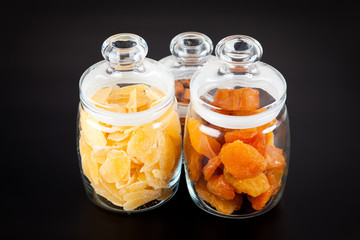 Glass jars with dried fruits (pineapples and peaches) and almonds on black background