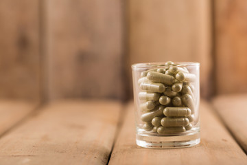 Fototapeta na wymiar Capsule green herbs in glass with wooden background