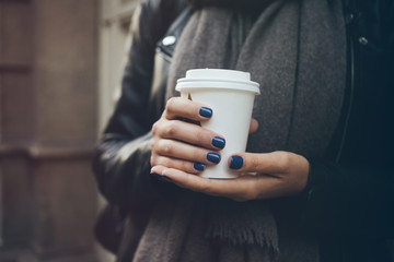 Young woman is drinking specialty coffee on the street while walking on cold winter day. Close-up of hands with white take away cup of hot coffee. Copy-space blank 