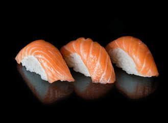Three sushi rolls lie on a black background with reflection. Fig