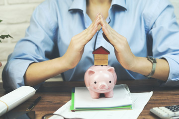 woman holding home or house model and piggy bank