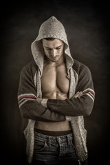 Confident, attractive young man with open vest on muscular torso, ripped abs and pecs. On dark...