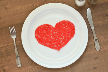 Red heart on a white plate, knife, fork and candles on the table. Valentine's Day.