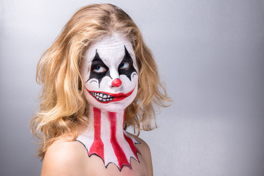 Portrait d'une jeune fille blonde maquillée en joker avec un faux sourire de profil, les yeux en l'air