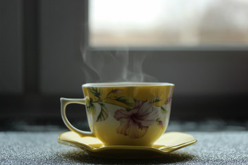 Beautiful and hot cup of coffee with saucer near the window early at the morning
