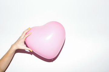 Pink heart baloon in hand on white wall