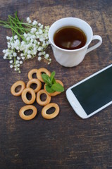 Bouquet of flowers and cup of tea on a wooden table with phone with a blank screen