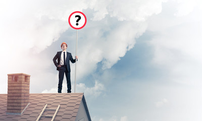 Businessman on brick house roof showing banner with question mark