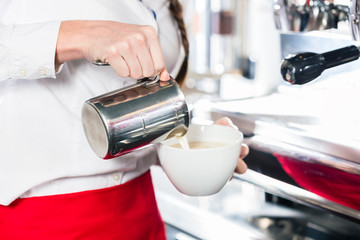 Close-up of the hands of a waitress pouring milk into a coffee c
