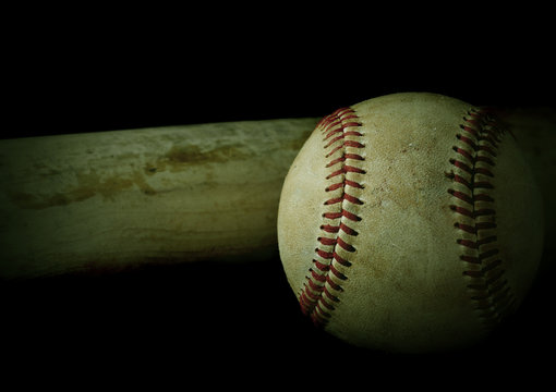 Low key image of old baseball and bat showing pine tar residue on black background. Vintage filter applied