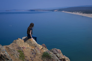 Fototapeta na wymiar Романтичная девушка сидит на краю обрыва скалы озера Байкал.