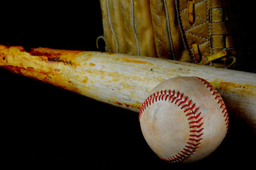 Low key image of old baseball and bat showing pine tar residue on black background. A baseball mitt is in the background. Shallow depth of field
