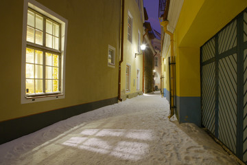 Narrow illuminated street in old town at night. Snow winter view.
