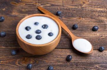 White yogurt in natural wooden bowl with blueberries and wooden