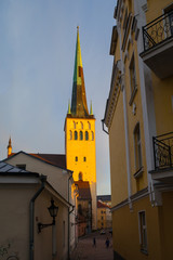 Sunset in old town. People are walking along narrow streets. St. Olaf (Oleviste) church shining in...