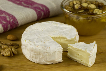 Brie cheese and a slice on a wooden board with nuts, honey. Italian, French cheese.